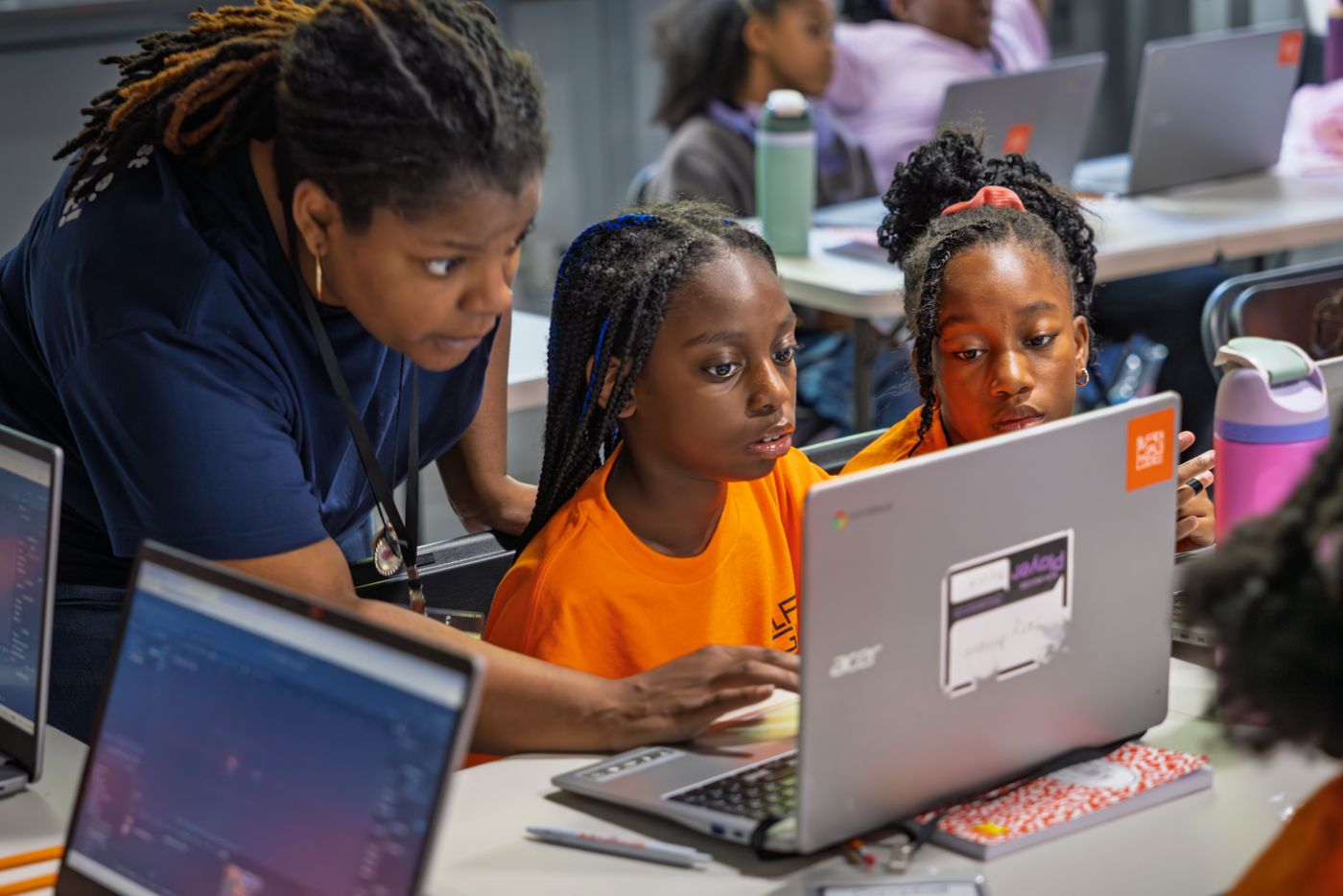 An instructor helps two students working on a laptop together